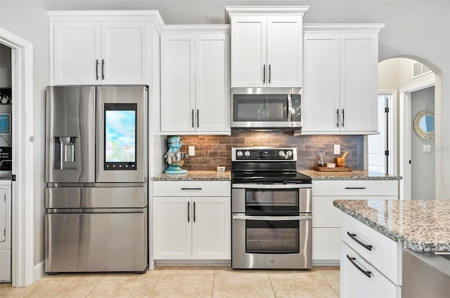 kitchen with light stone counters, tasteful backsplash, stainless steel appliances, white cabinets, and light tile patterned floors