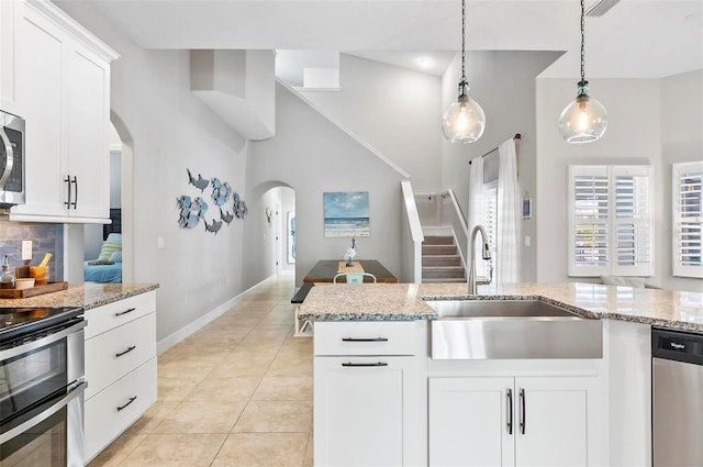 kitchen featuring pendant lighting, a sink, stainless steel appliances, arched walkways, and light tile patterned flooring