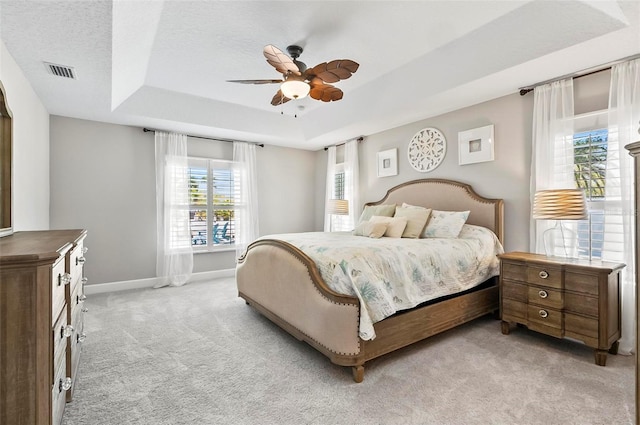 bedroom with visible vents, baseboards, light colored carpet, a tray ceiling, and a textured ceiling