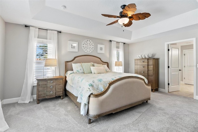 carpeted bedroom with a tray ceiling, baseboards, and ceiling fan