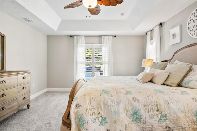 bedroom featuring visible vents, light colored carpet, a raised ceiling, and baseboards