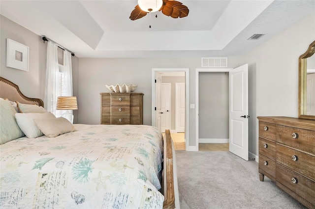 bedroom with visible vents, light carpet, a raised ceiling, and baseboards