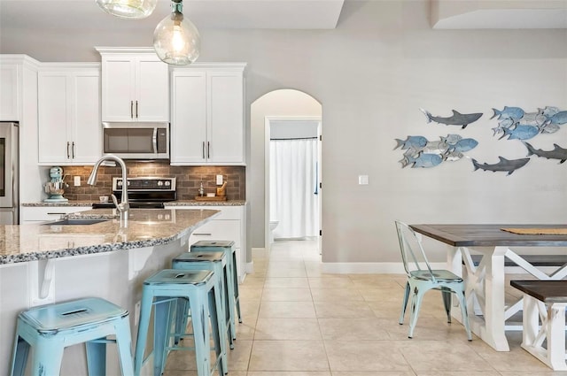 kitchen with tasteful backsplash, light stone counters, appliances with stainless steel finishes, arched walkways, and a sink