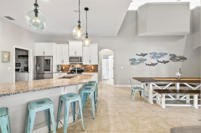 kitchen with visible vents, arched walkways, a sink, decorative backsplash, and appliances with stainless steel finishes