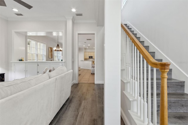 living area with stairway, visible vents, dark wood finished floors, crown molding, and a notable chandelier