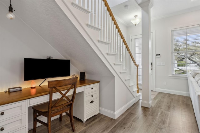 office space featuring baseboards, built in desk, light wood finished floors, and ornamental molding