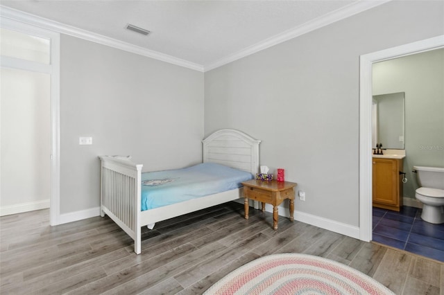 bedroom featuring wood finished floors, visible vents, baseboards, ensuite bathroom, and crown molding