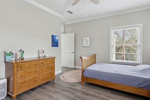 bedroom featuring visible vents, ornamental molding, a ceiling fan, wood finished floors, and baseboards