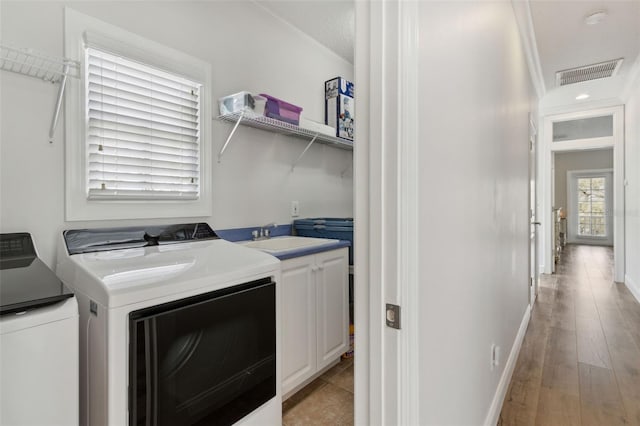 clothes washing area featuring visible vents, washing machine and clothes dryer, cabinet space, a sink, and light wood-type flooring