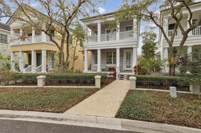 neoclassical home featuring a fenced front yard, a balcony, a porch, and stucco siding