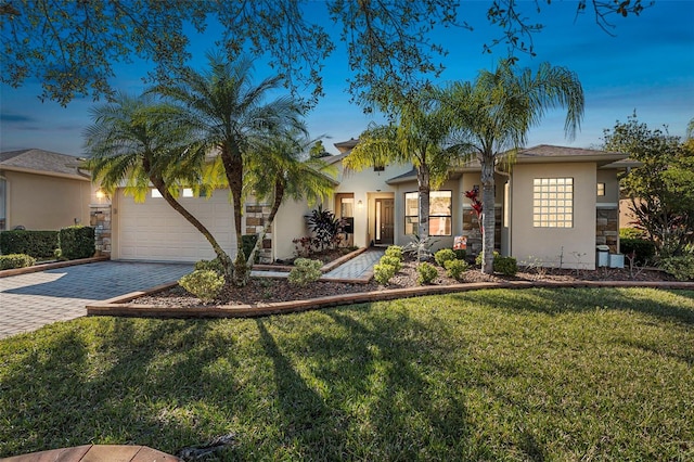 view of front of property featuring an attached garage, stone siding, decorative driveway, stucco siding, and a front lawn