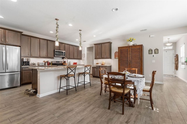 interior space featuring recessed lighting, a breakfast bar, appliances with stainless steel finishes, light wood finished floors, and an island with sink