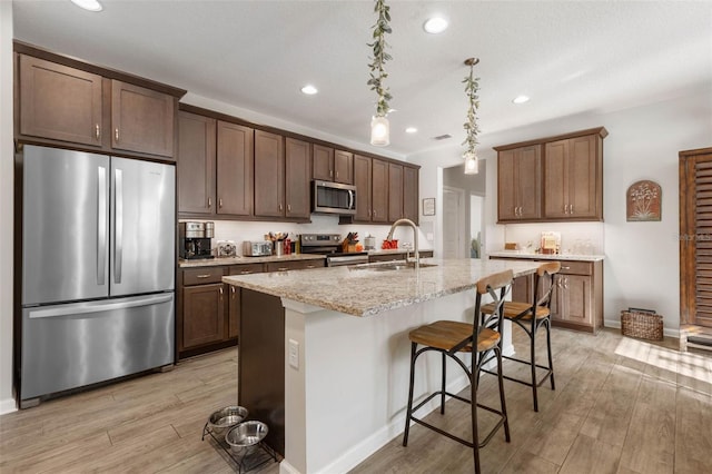 kitchen with a breakfast bar area, stainless steel appliances, light wood-style flooring, a sink, and light stone countertops