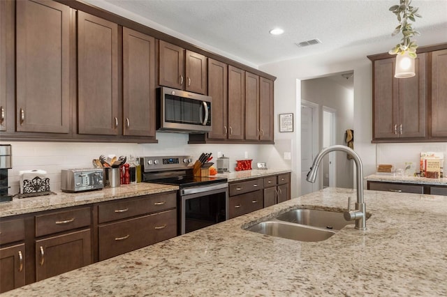 kitchen with visible vents, backsplash, appliances with stainless steel finishes, a sink, and light stone countertops