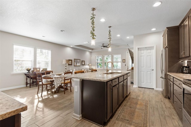 kitchen with light wood-type flooring, freestanding refrigerator, a sink, and dark brown cabinets