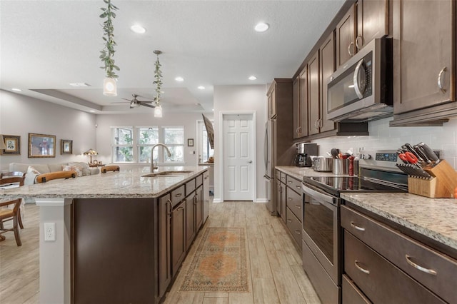 kitchen featuring tasteful backsplash, a kitchen island with sink, appliances with stainless steel finishes, and dark brown cabinets