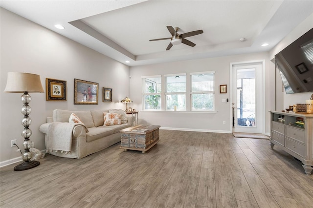 living area featuring a tray ceiling, recessed lighting, wood finished floors, and baseboards