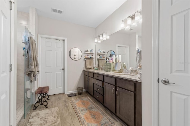 full bathroom featuring visible vents, a sink, a tile shower, and wood finished floors