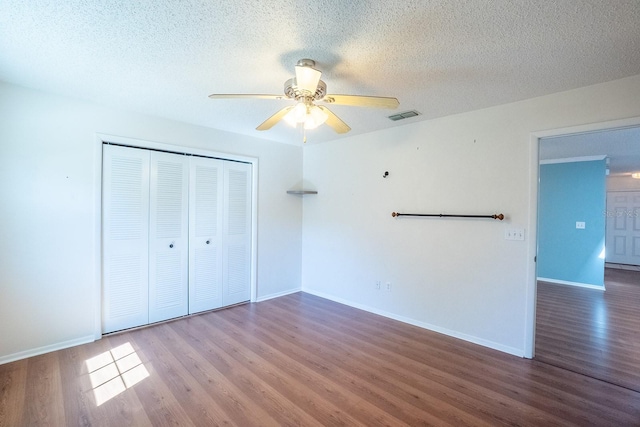 unfurnished bedroom featuring visible vents, a textured ceiling, wood finished floors, a closet, and baseboards