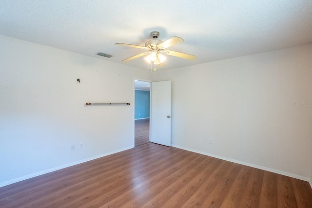 empty room with wood finished floors, visible vents, baseboards, ceiling fan, and a textured ceiling