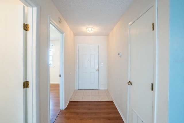 corridor with visible vents, baseboards, a textured ceiling, and wood finished floors