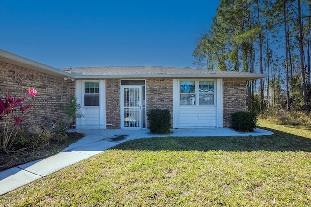 view of exterior entry with a yard and brick siding