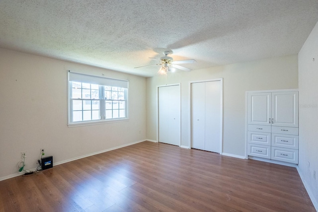 unfurnished bedroom with baseboards, two closets, wood finished floors, and a ceiling fan