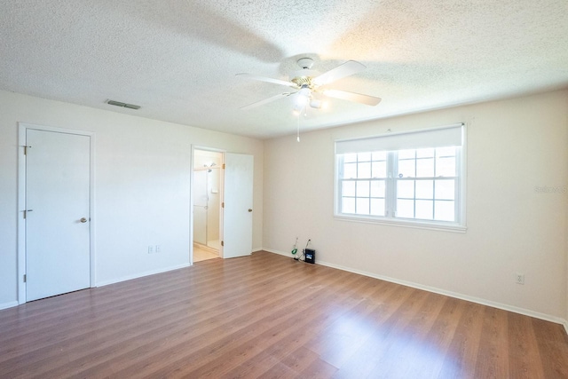 unfurnished bedroom featuring baseboards, wood finished floors, visible vents, and a textured ceiling