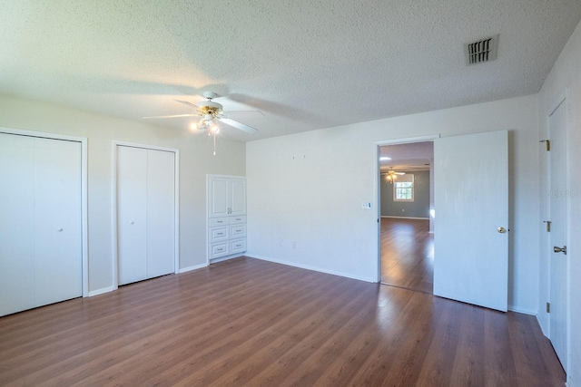 unfurnished bedroom featuring visible vents, multiple closets, a ceiling fan, a textured ceiling, and dark wood-style floors