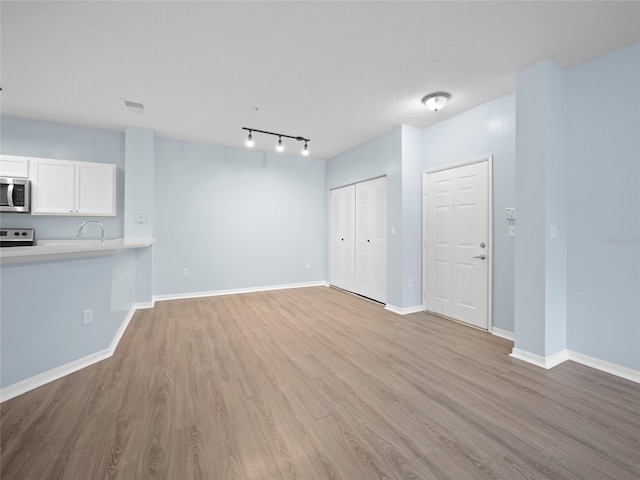 unfurnished living room featuring visible vents, a sink, light wood-style flooring, and baseboards