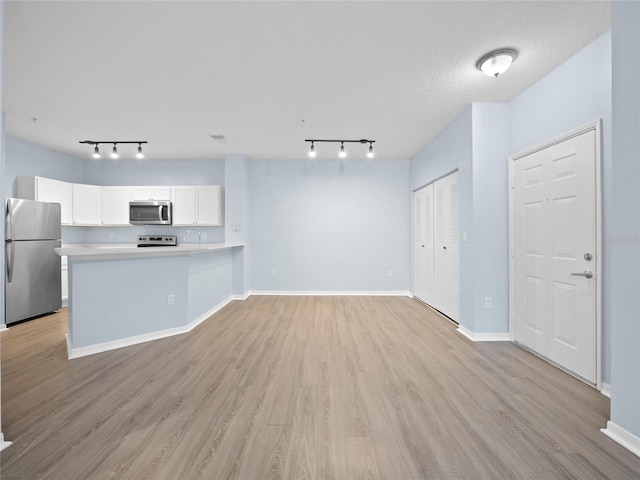 unfurnished living room with rail lighting, baseboards, a textured ceiling, and light wood finished floors