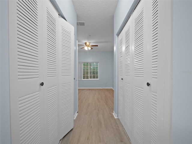 corridor with a textured ceiling, light wood-type flooring, visible vents, and baseboards