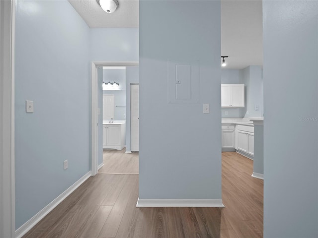 hallway with a textured ceiling, baseboards, and wood finished floors