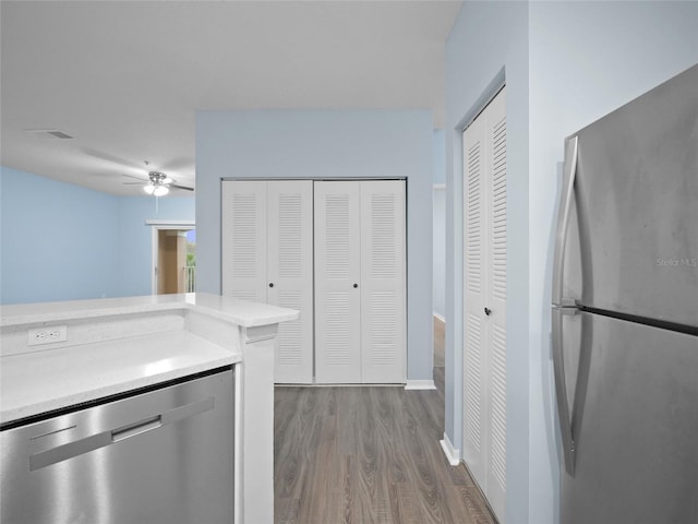 kitchen with wood finished floors, a ceiling fan, baseboards, light countertops, and appliances with stainless steel finishes