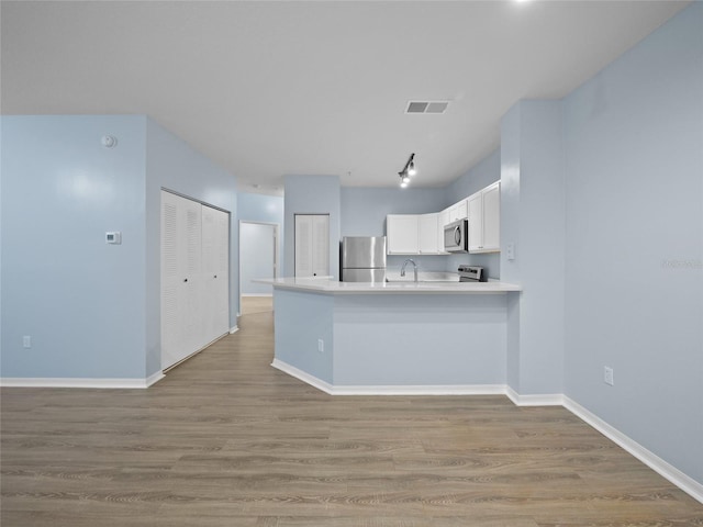 kitchen with stainless steel appliances, a peninsula, wood finished floors, visible vents, and white cabinets