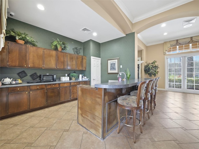 kitchen featuring crown molding, visible vents, a breakfast bar area, and french doors