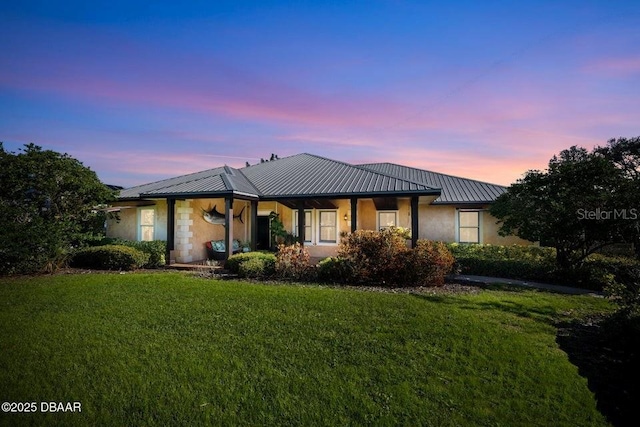 back of house at dusk with a standing seam roof, metal roof, a lawn, and stucco siding