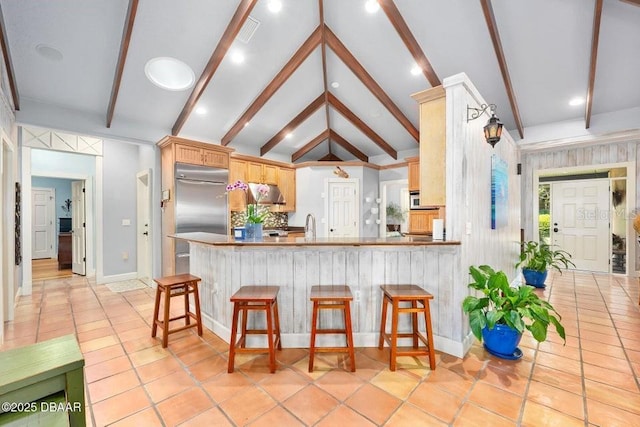 kitchen with lofted ceiling with beams, stainless steel built in fridge, a peninsula, and a breakfast bar area