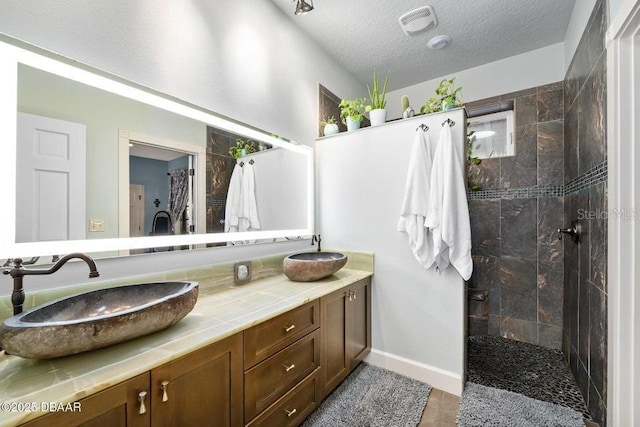 full bath featuring a textured ceiling, double vanity, walk in shower, and a sink