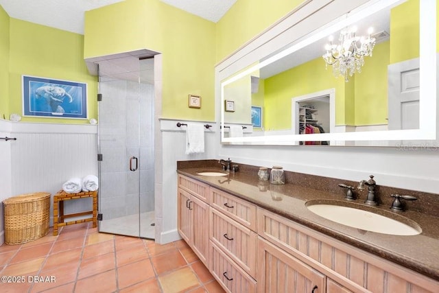 bathroom with a notable chandelier, a shower stall, a sink, and wainscoting