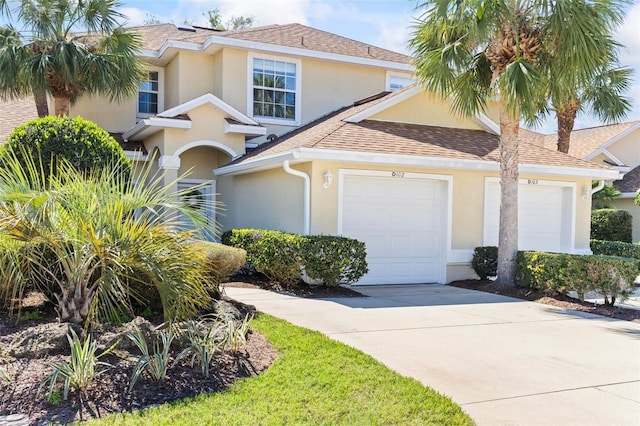 traditional-style home featuring an attached garage, roof with shingles, concrete driveway, and stucco siding