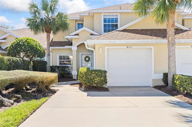 traditional-style home featuring an attached garage, a shingled roof, concrete driveway, and stucco siding