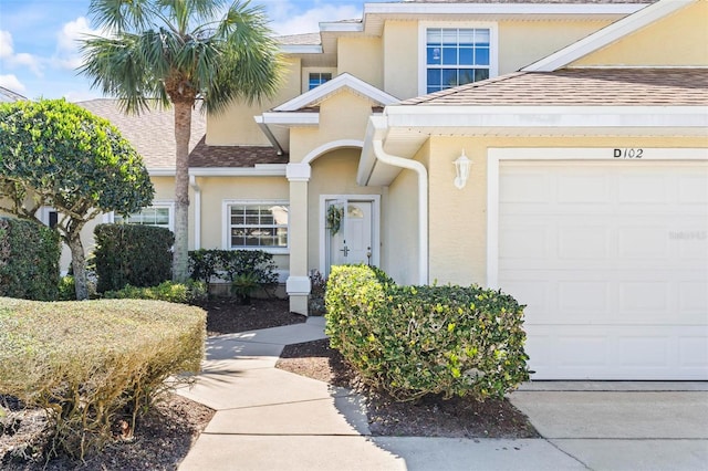 doorway to property featuring a garage, a shingled roof, and stucco siding