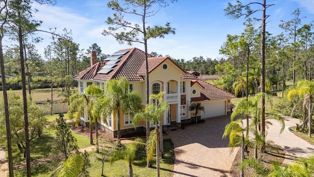 view of home's exterior with a garage, solar panels, a tile roof, a chimney, and decorative driveway