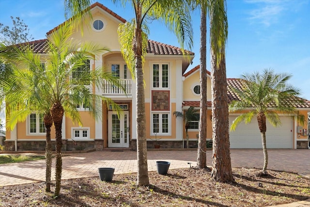 mediterranean / spanish-style home with french doors, a tile roof, stucco siding, an attached garage, and a balcony