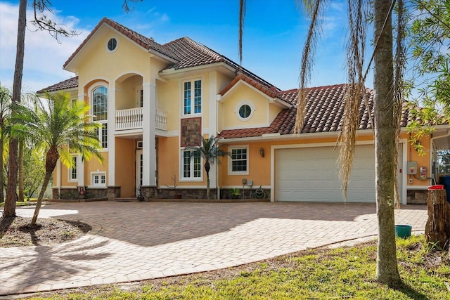 mediterranean / spanish-style house featuring an attached garage, a tile roof, stone siding, decorative driveway, and stucco siding