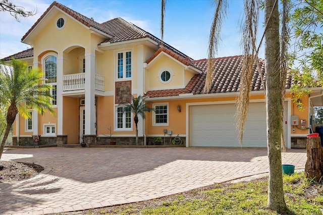 view of front of home with stucco siding, a balcony, a garage, driveway, and a tiled roof