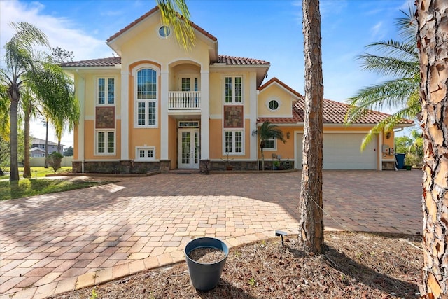 mediterranean / spanish house with stone siding, french doors, an attached garage, and stucco siding