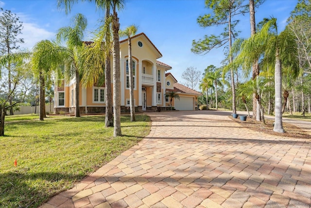 mediterranean / spanish home with a garage, decorative driveway, a front lawn, and stucco siding