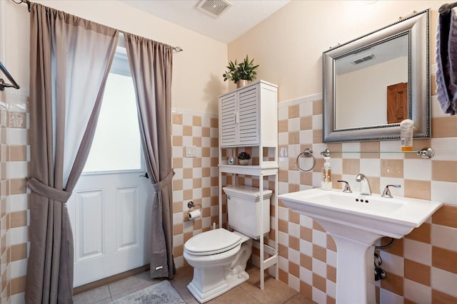 half bath with toilet, tile walls, visible vents, and tile patterned floors